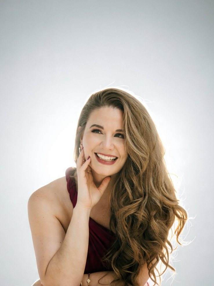 Christi Michelle laughing, seated in a burgundy gown against bright light